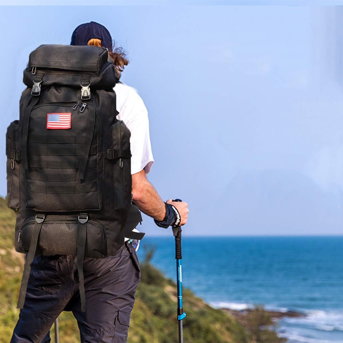 Person with a large black backpack and American flag patch, standing on a cliff overlooking the ocean.