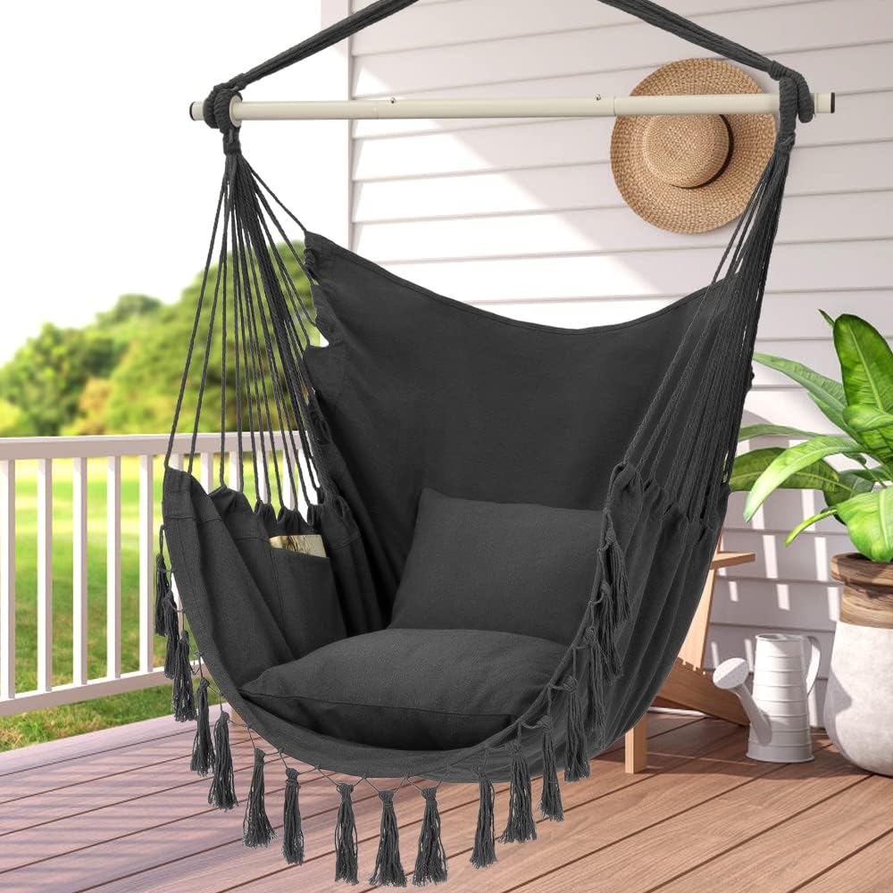 Black hammock chair with tassels on a wooden deck with a white railing and greenery in the background.