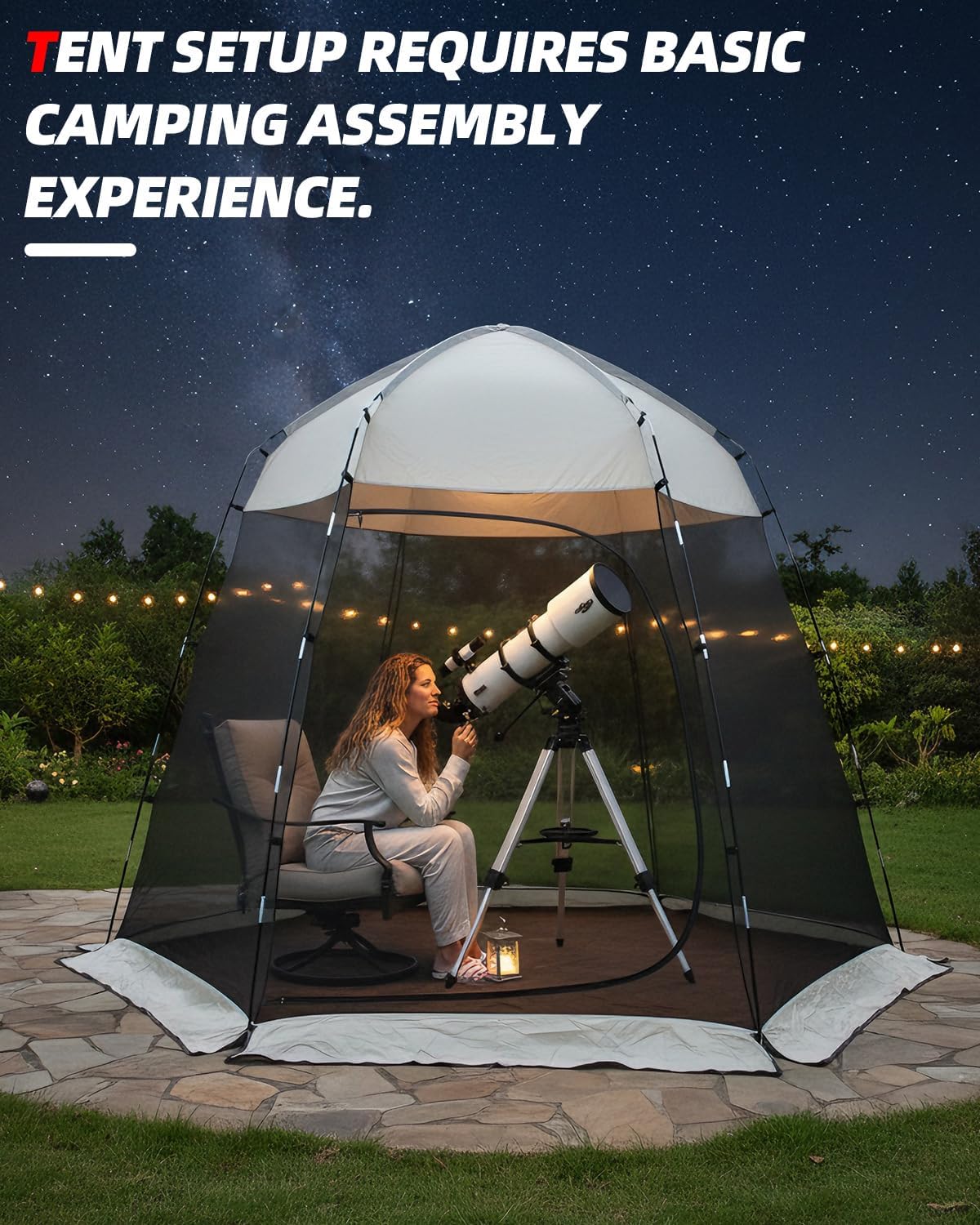 A dome-style camping tent with a transparent mesh enclosure is set up outdoors at night on a stone patio. A woman sits inside under the tent next to a telescope.