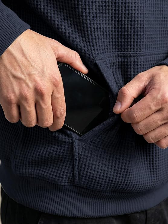 Close-up of a person wearing a navy blue waffle-knit hoodie, showing hands pulling a black smartphone out of a front pocket.
