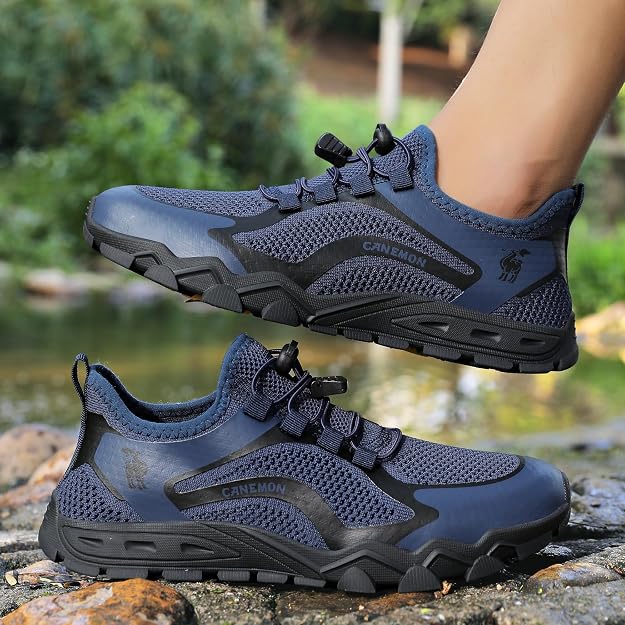 A pair of dark blue and black outdoor hiking shoes, with one shoe shown on a person's foot and the other resting on rocks by a stream. The brand name CANEMON is visible on the side of the shoes.