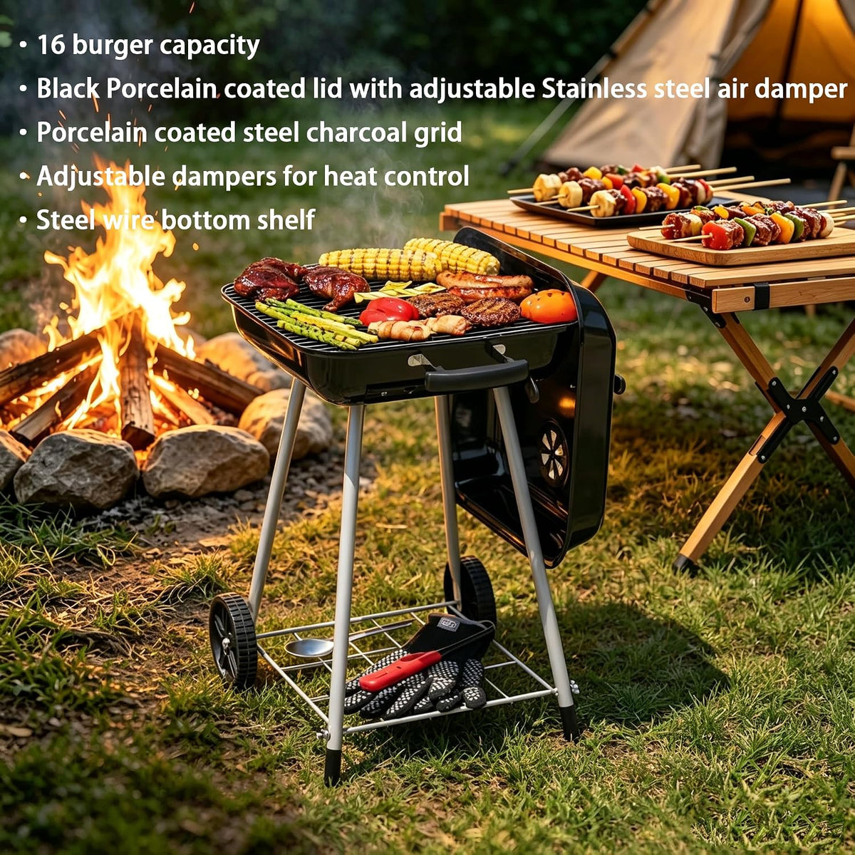 A black portable charcoal grill with a porcelain-coated lid and wheels is shown outdoors on grass beside a campfire and a folding table with skewered food. Text on the left lists features such as 16 burger capacity, black porcelain-coated lid, adjustable stainless steel air damper, porcelain-coated steel charcoal grid, adjustable dampers for heat control, and steel wire bottom shelf.