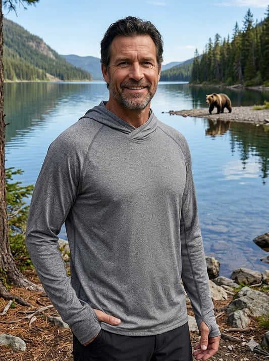 Man in gray hoodie standing by a lake with a bear in the background Biggreenbear.com
