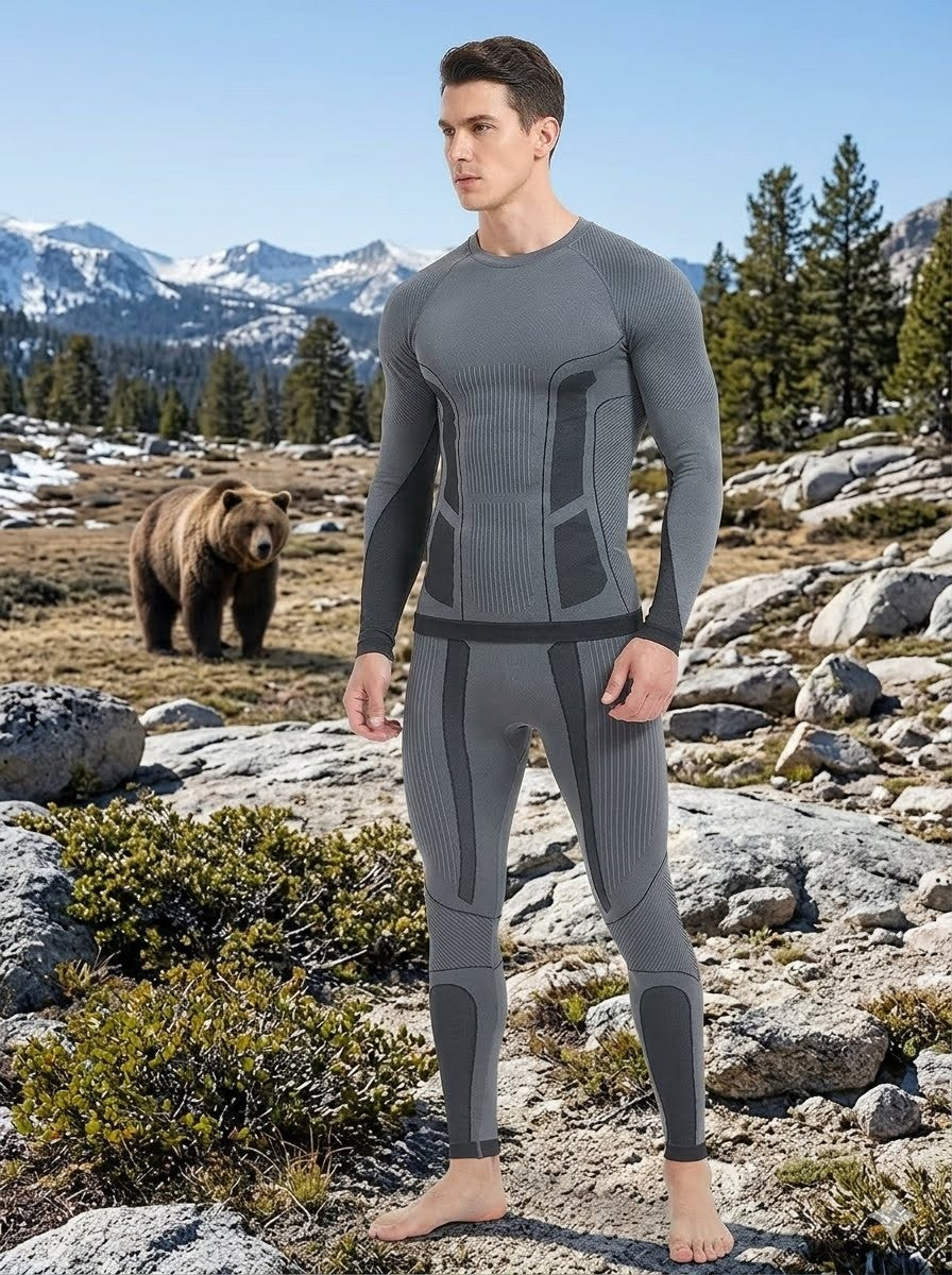 Man wearing gray compression suit standing in a mountainous landscape with a bear in the background.