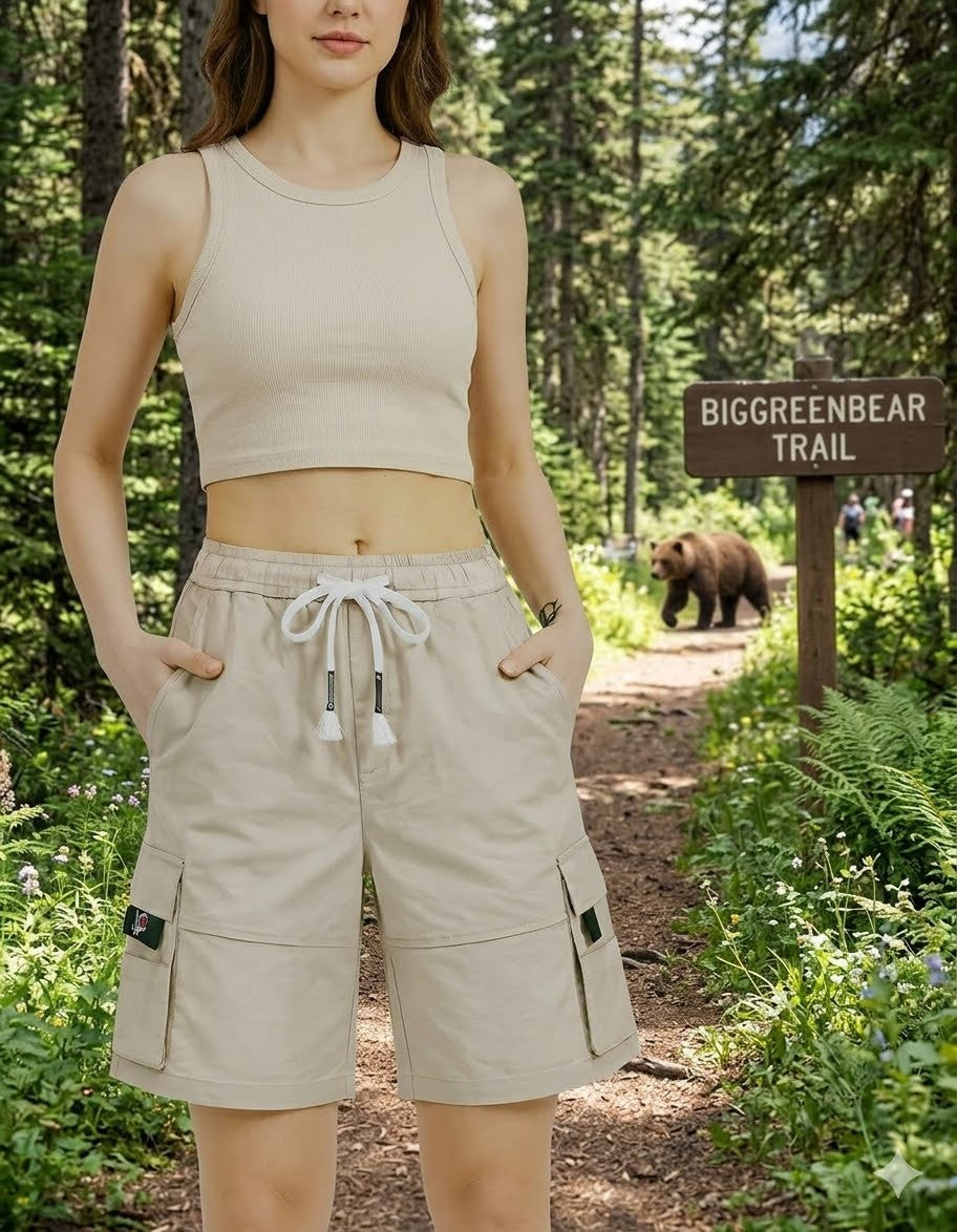 Woman in beige sleeveless top and shorts standing on a trail with a bear and sign in the background big green bear