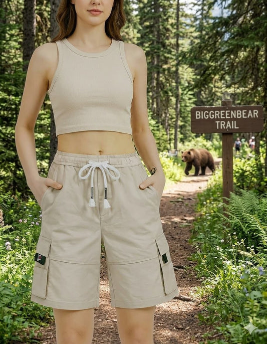 Woman in beige sleeveless top and shorts standing on a trail with a bear and sign in the background big green bear