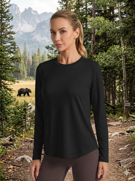 A woman wearing a black long-sleeve athletic top stands on a forest trail with mountains and trees in the background. Big green bear