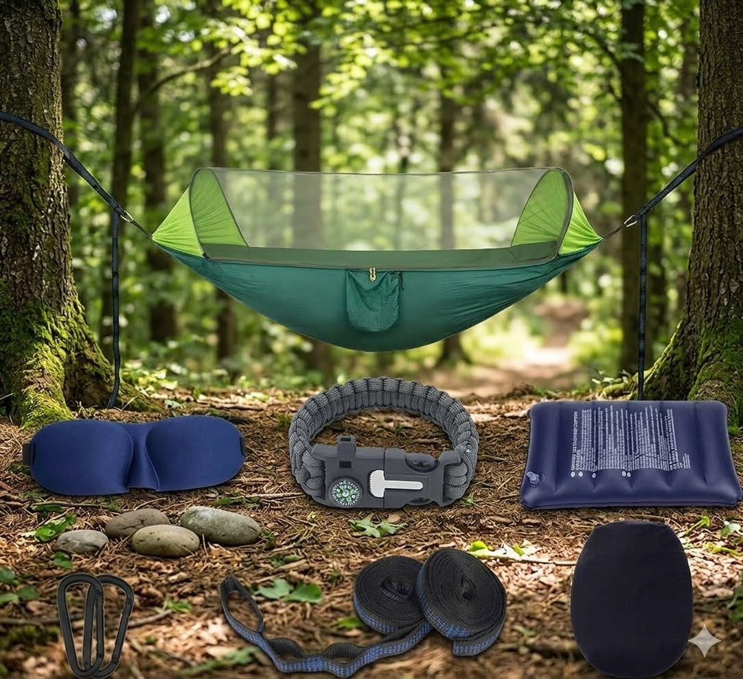 A camping hammock set displayed in a forest setting, with the hammock suspended between two trees and additional included items arranged on the forest floor below, including a mosquito net, sleeping pad, pillow, straps, and carabiner.