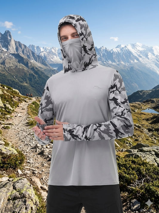 A man wearing a light gray long-sleeve athletic shirt with a black and white camouflage hood and face mask, standing on a mountain trail with snowy peaks in the background. big green bear