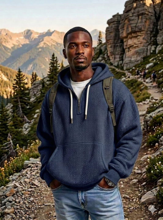 A man wearing a navy blue waffle-knit pullover hoodie with white drawstrings, standing on a mountain hiking trail. big green bear