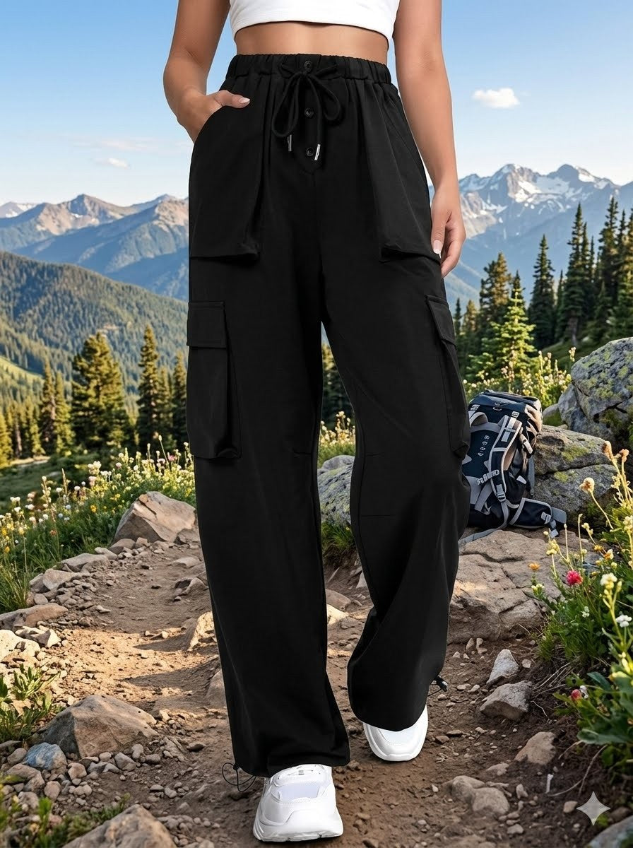 A person wearing black wide-leg cargo pants with a drawstring waist, standing on a mountain trail with a backpack nearby. big green bear