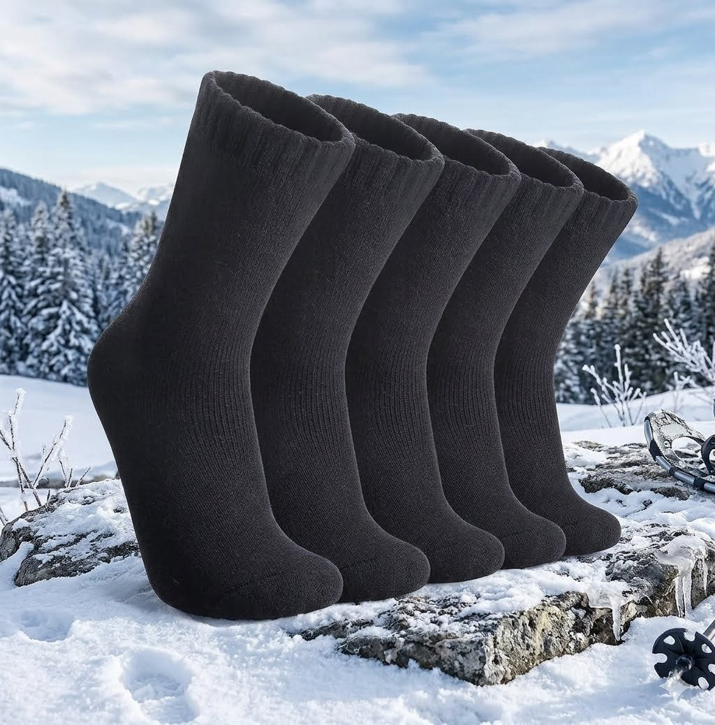 Four black mid-calf knit socks arranged in a row on a snowy rock, with a snowy mountain landscape in the background. big green bear
