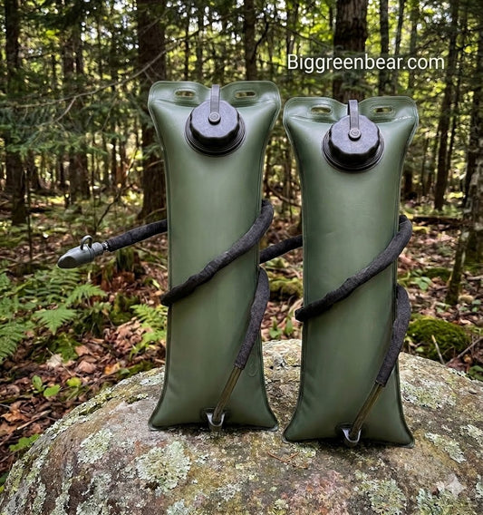 Two olive green inflatable water bottles with black straws, standing on a mossy rock in a forest setting. A watermark 'Biggreenbear.