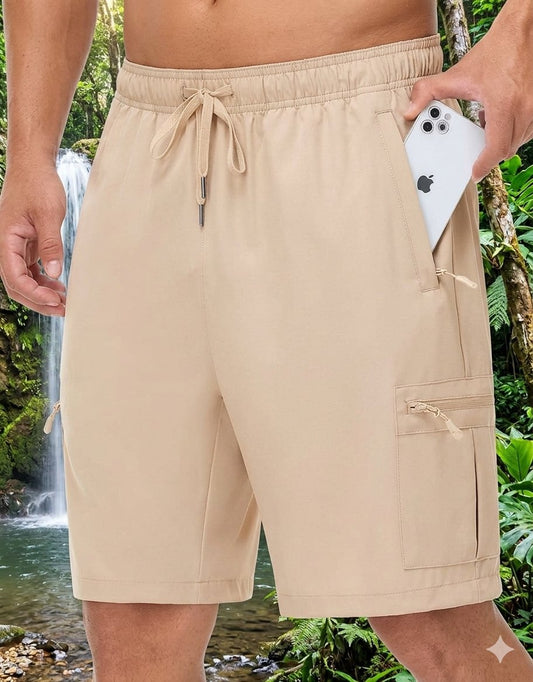 Beige men's swim trunks with a drawstring waist and side cargo pockets, shown on a model in a tropical outdoor setting with a waterfall in the background. biggreenbear.com big green bear