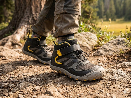 A close-up of a person hiking on a rocky forest trail, wearing black and gray hiking boots with bright yellow accents and olive cargo pants. big green bear biggreenbear.com