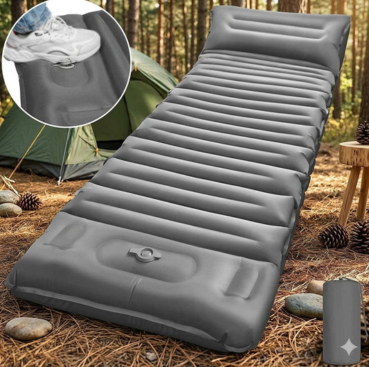 Gray inflatable camping sleeping pad laid out on forest ground with pine needles, stones, and a tent in the background. A circular inset shows a white sneaker stepping onto the pad to demonstrate its thickness and comfort. big green bear biggreenbear.com