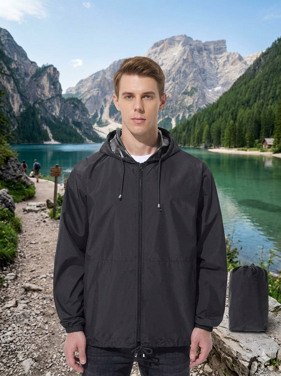 A man wearing a black hooded rain jacket stands outdoors in front of a scenic mountain lake landscape, with a matching black pouch placed beside him. big green bear biggreenbear.com