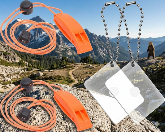 Outdoor emergency preparedness set featuring two orange whistle paracord lanyards with black snap buttons and two clear ID tags on silver ball chains, shown against a mountain trail background with a bear silhouette. big green bear