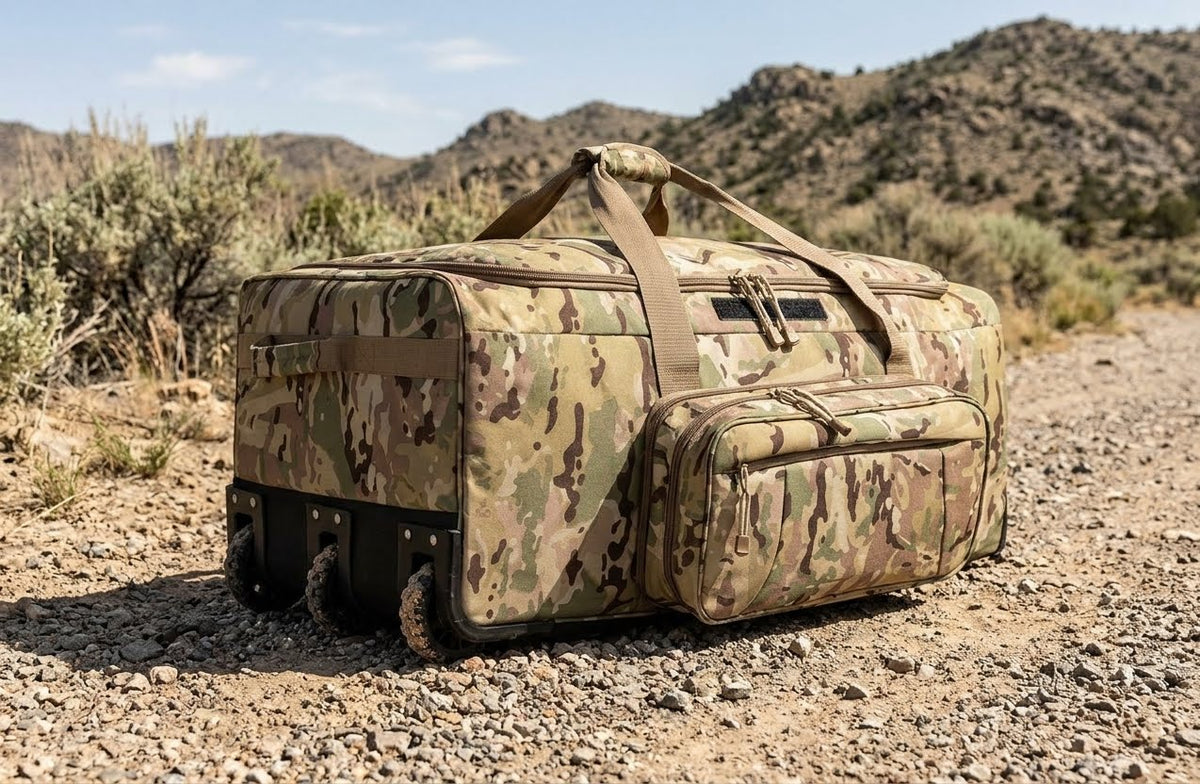 A large rolling duffel bag with a camouflage pattern sits on a gravel path in a desert landscape with mountains in the background. big green bear biggreenbear.com