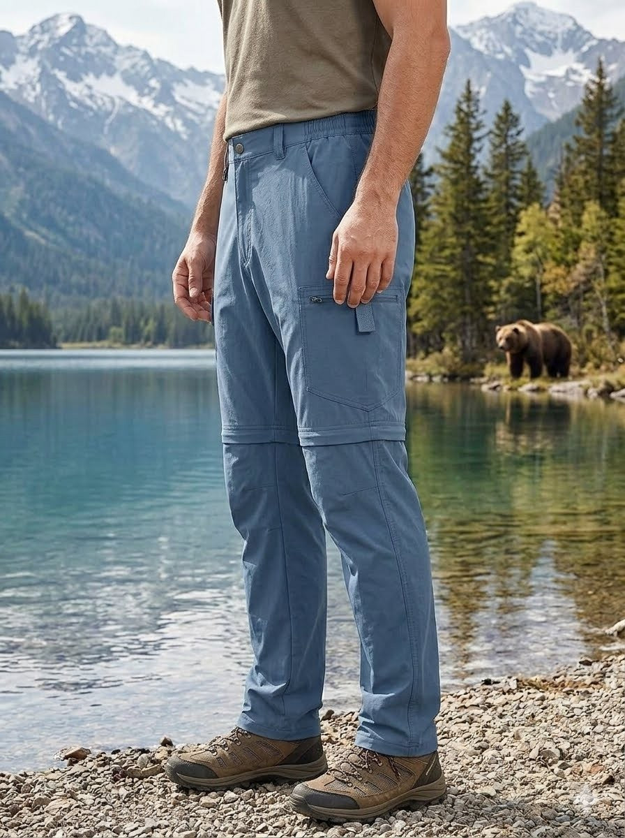 Person wearing blue hiking pants standing by a lake with a bear in the background