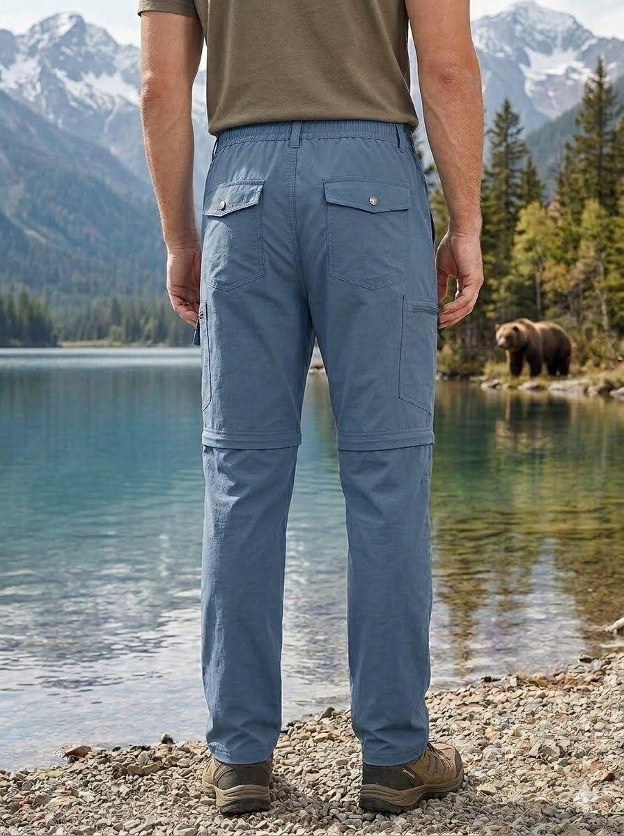 Person wearing blue pants standing by a lake with mountains and a bear in the background