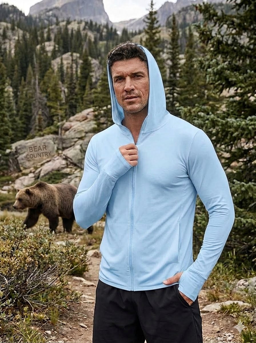Man wearing a light blue hoodie in a mountainous forest with a bear in the background Biggreenbear.com