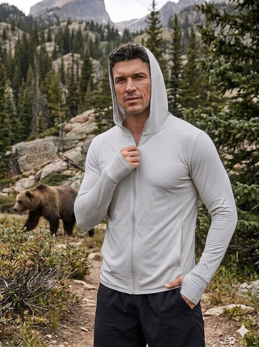Man in a gray hoodie standing in a mountainous area with a bear in the background Biggreenbear.com