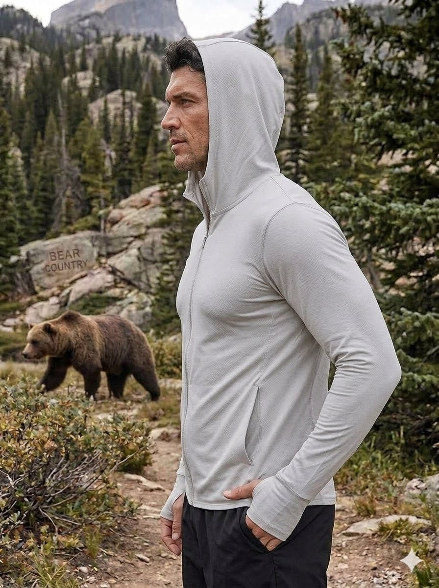 Person wearing a light gray hoodie in a mountainous area with a bear in the background
