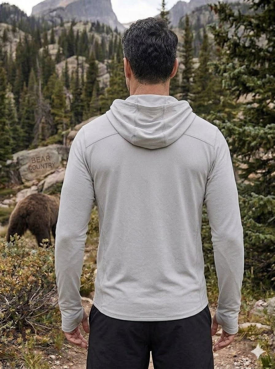 Person wearing a gray hoodie in a mountainous forest with a bear in the background