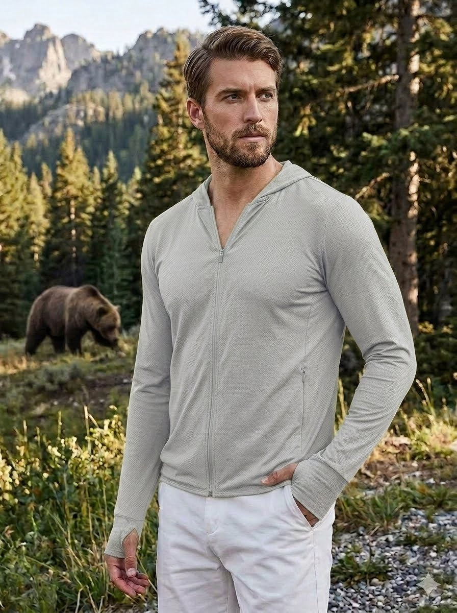 Man wearing a light gray zip-up hoodie and white pants standing in a forest with a bear in the background. Biggreenbear.com