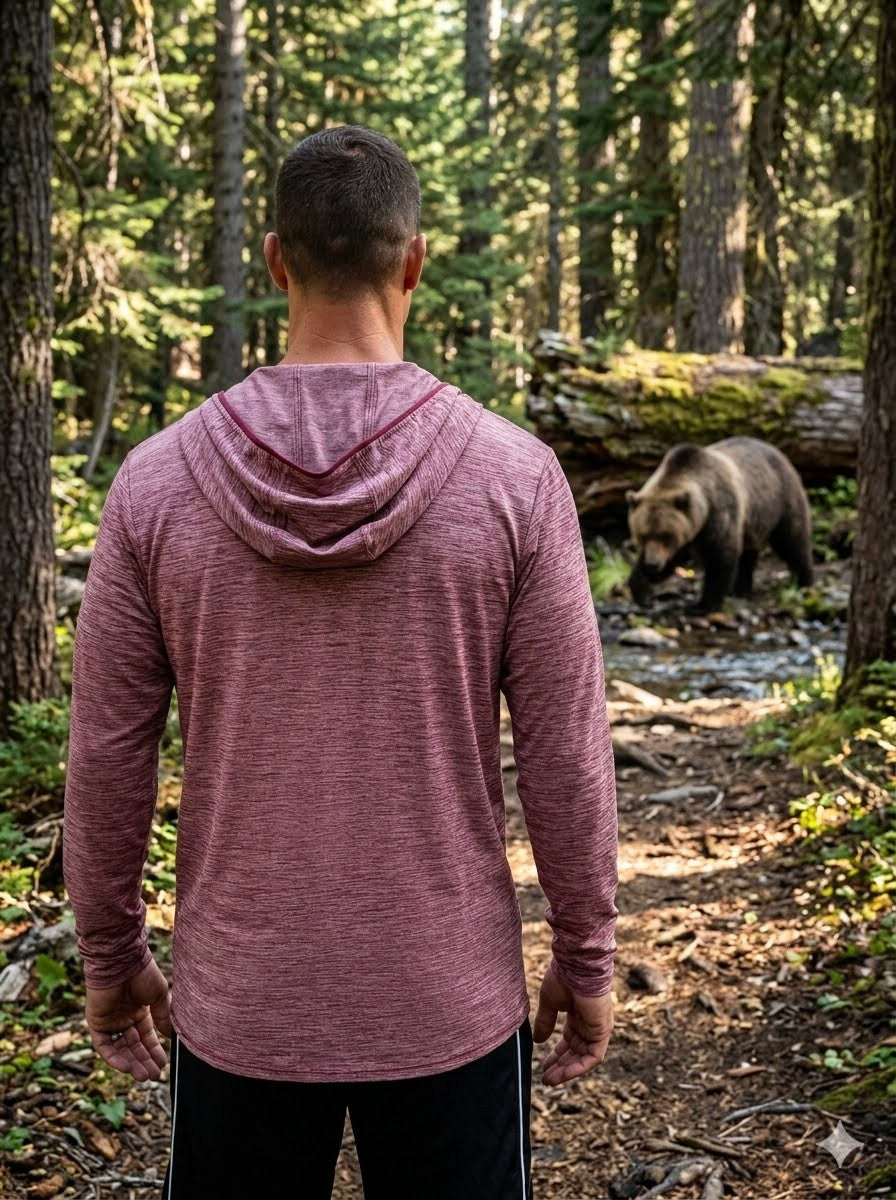 Person wearing a maroon hoodie in a forest with a bear nearby