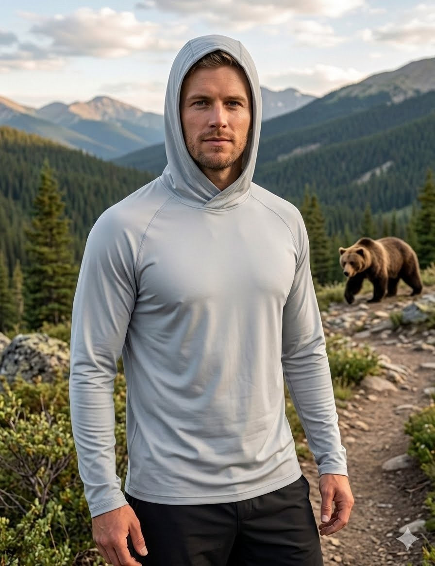 Man wearing a light gray hoodie standing in a mountainous area with a bear in the background
