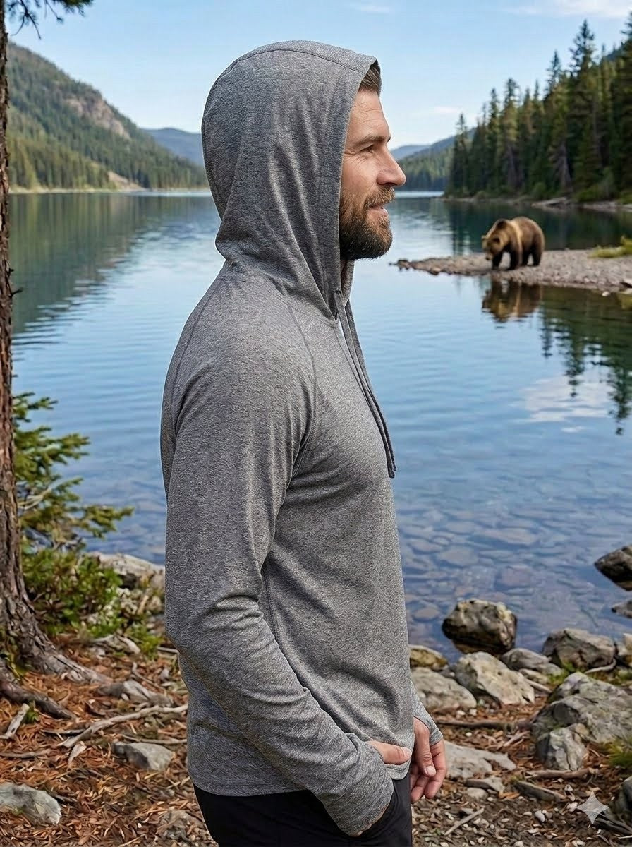 Man wearing a gray hoodie standing by a lake with a bear in the background