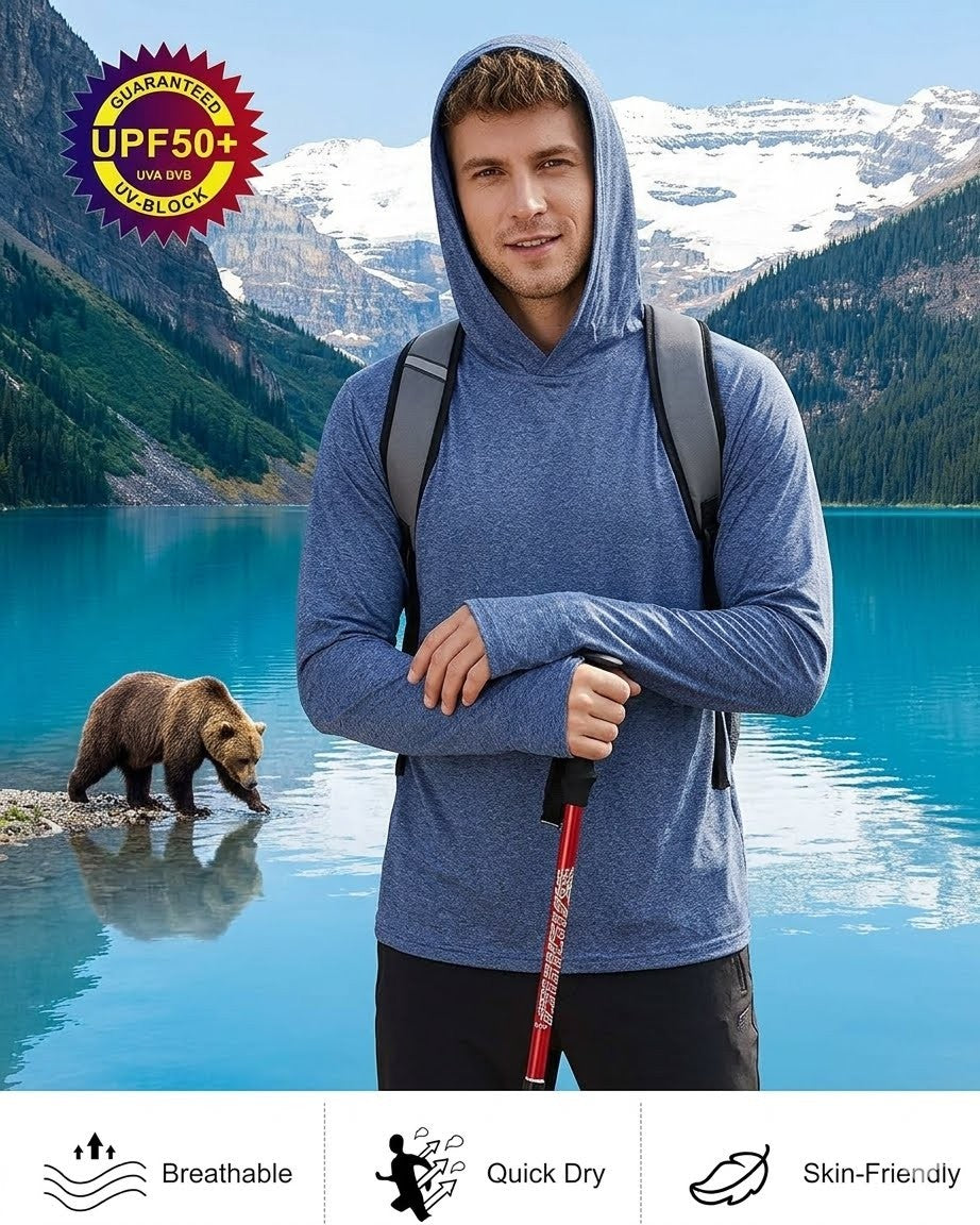Man in a blue hoodie with a backpack standing by a lake with a bear and mountains in the background.
