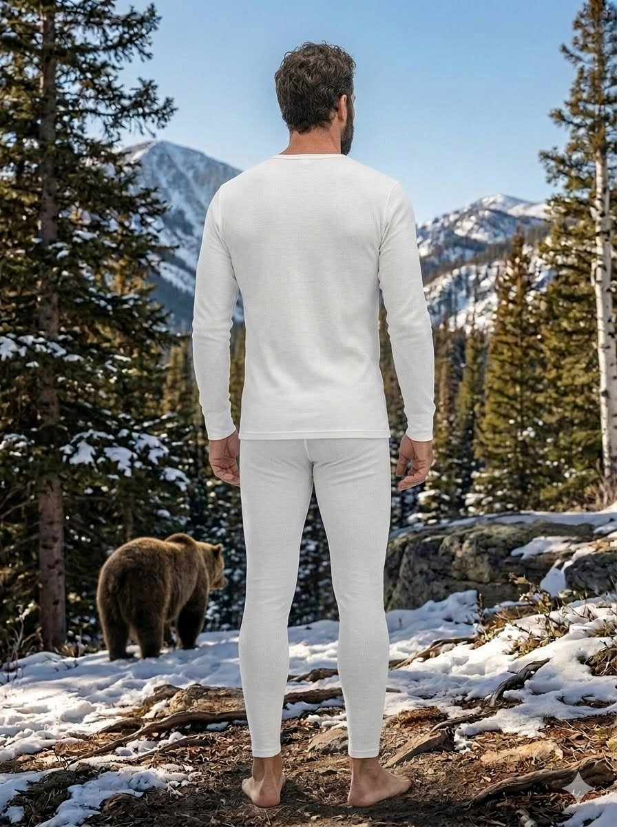 Man in white long-sleeve shirt and pants standing in a snowy forest with a bear nearby