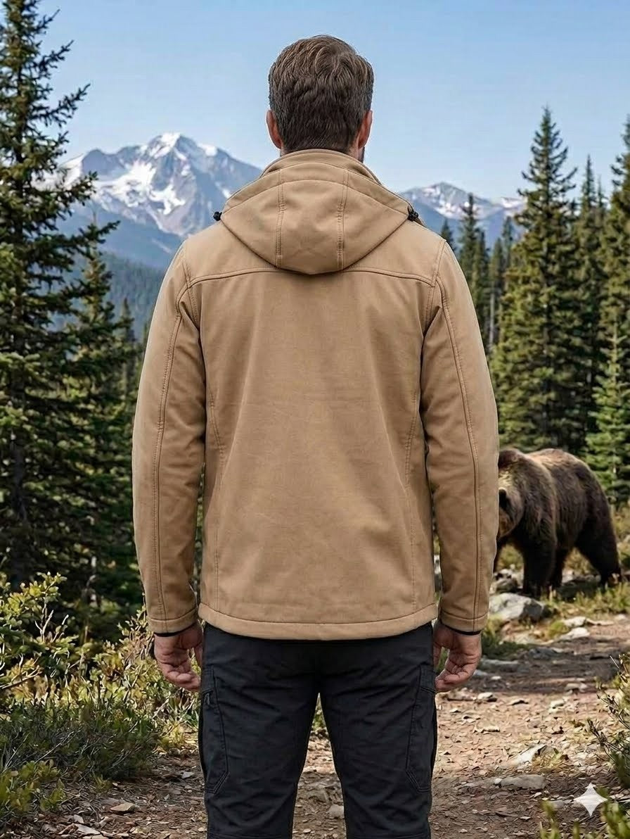 Man wearing a tan jacket in a forest with a bear in the background