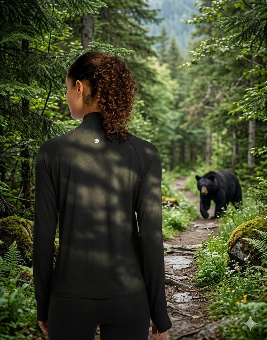 Person in black jacket walking through a forest with a bear on a path