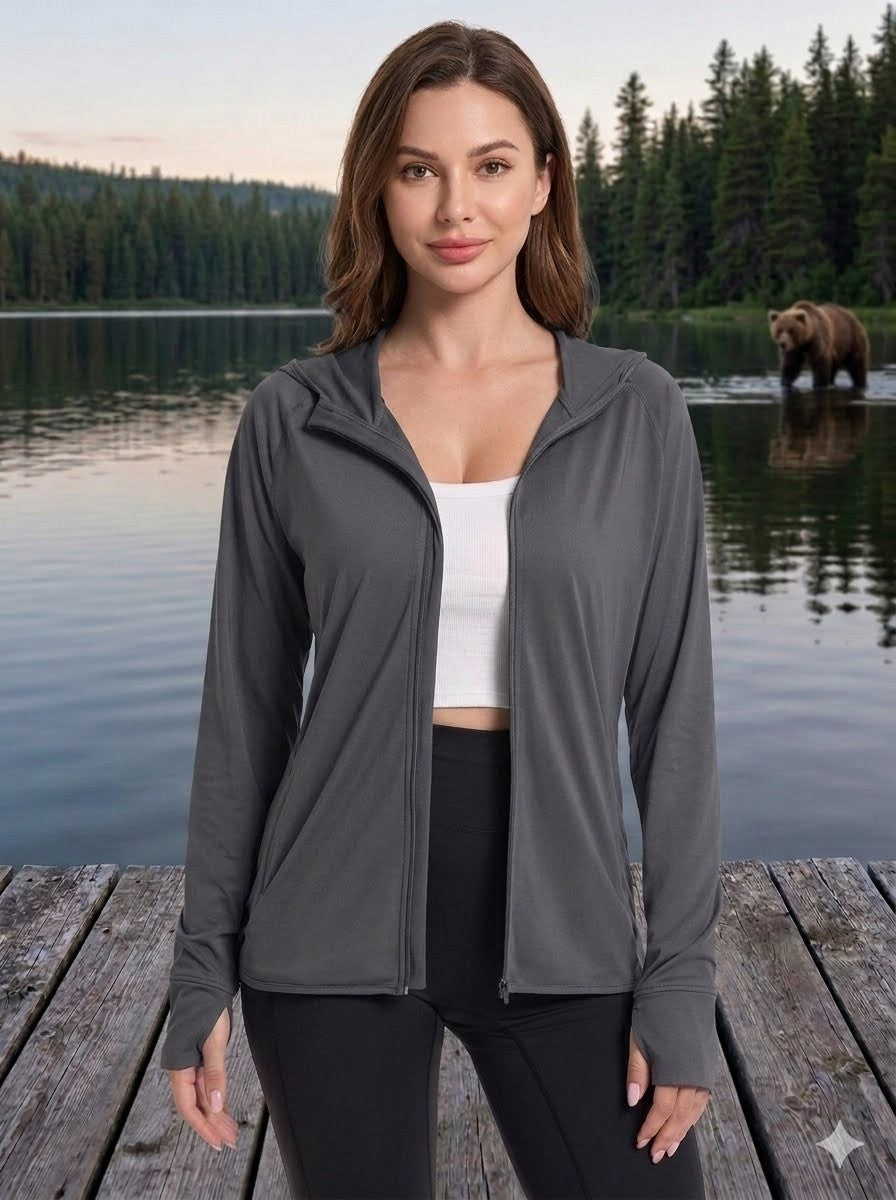 Woman wearing a gray zip-up jacket by a lake with a bear in the background big green bear
