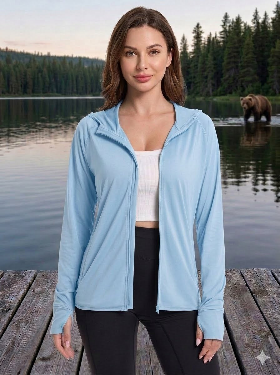 Woman wearing a light blue zip-up jacket standing on a wooden dock with a lake and bear in the background. big green bear