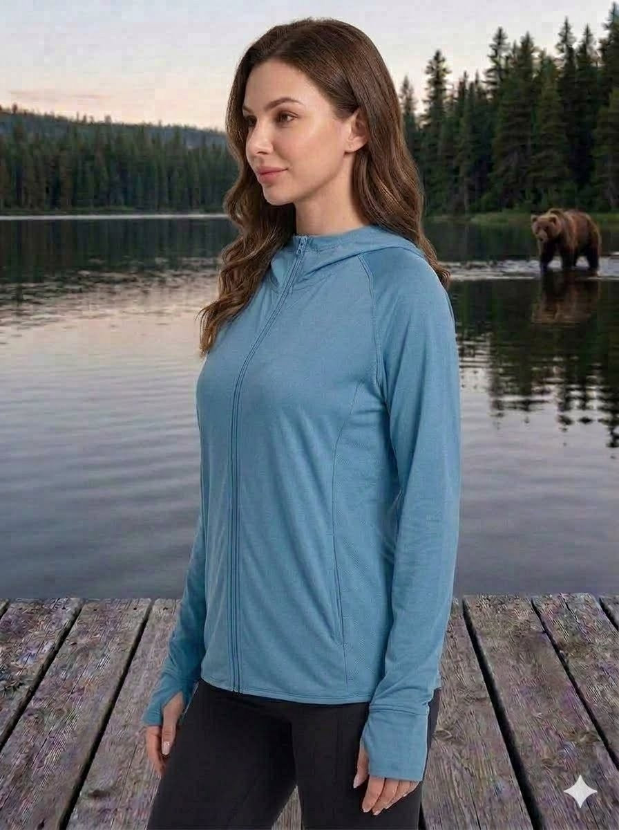 Woman in a blue jacket standing on a wooden dock by a lake with a bear in the background.