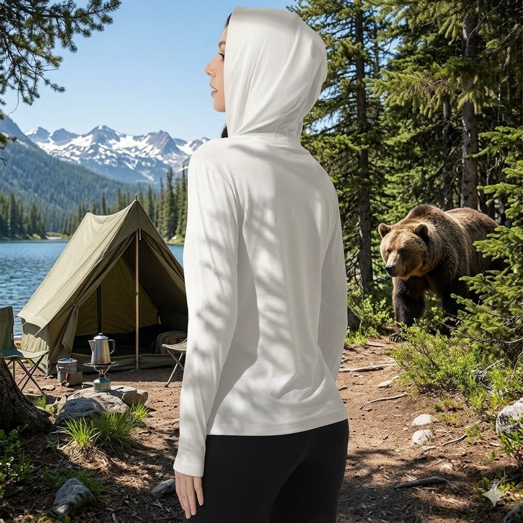 Person in a white hoodie standing near a tent with a bear in a forested area.