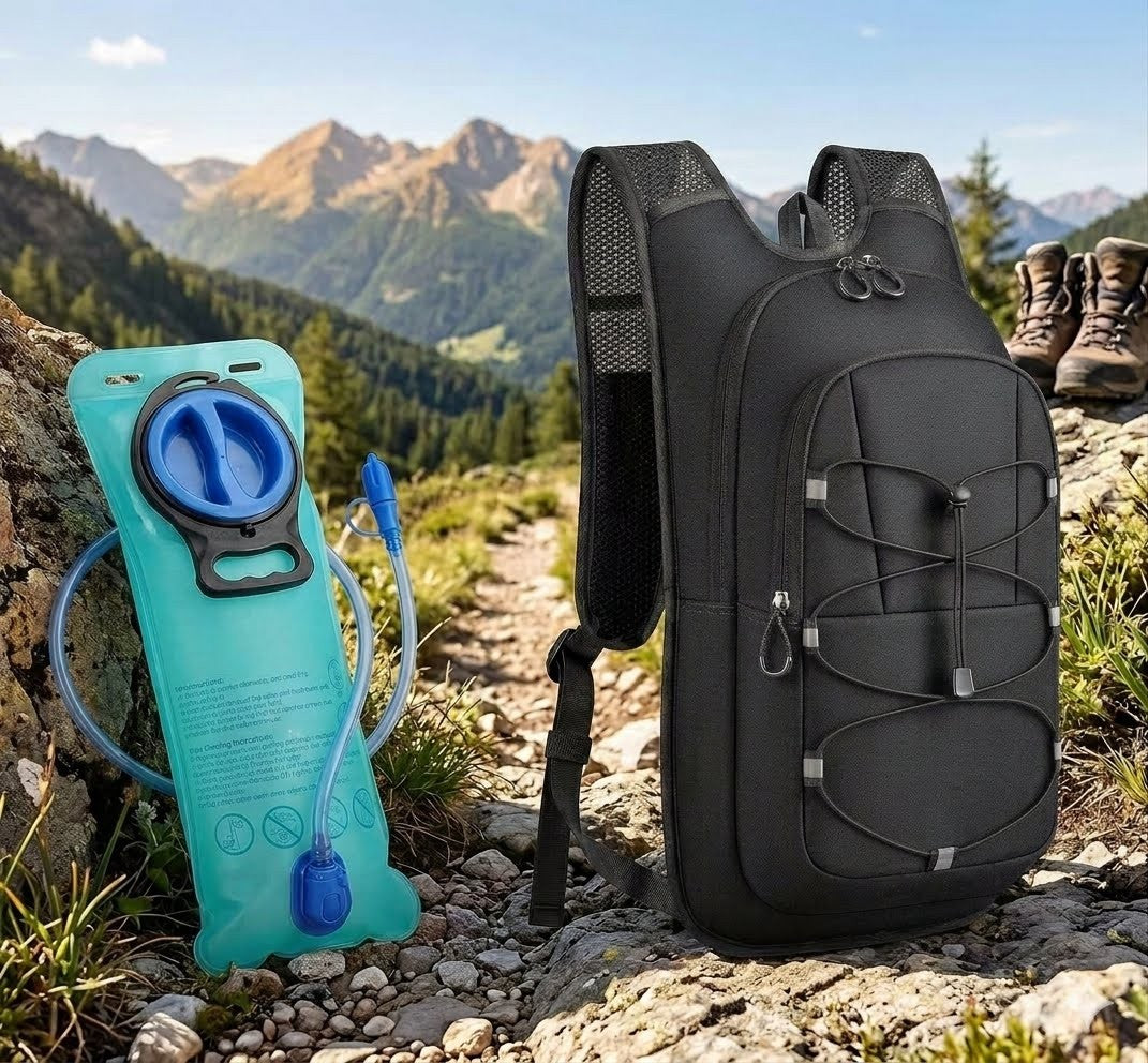 A black hydration backpack stands on a rocky mountain trail next to a turquoise hydration bladder with a blue drinking tube, with mountains in the background.