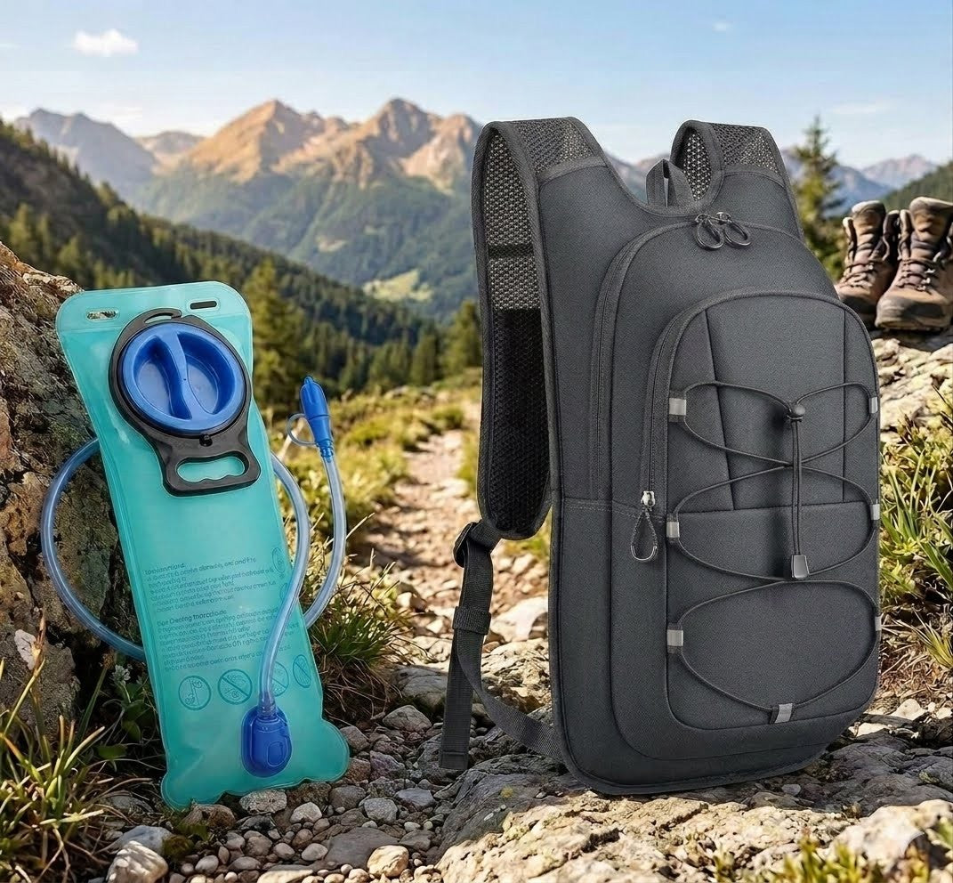 A dark gray hydration backpack stands on a rocky mountain trail next to a turquoise hydration bladder with a blue drinking tube, with mountains in the background.