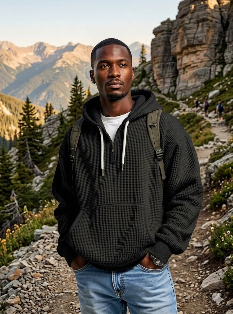 A man wearing a black textured waffle-knit pullover hoodie with white drawstrings, standing on a mountain hiking trail. big green bear