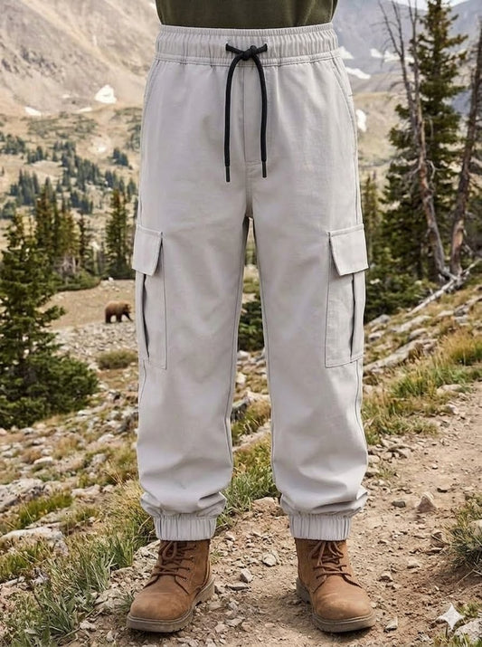 A person standing outdoors in a mountain landscape wearing light beige cargo jogger pants with a black drawstring waist and brown lace-up boots. big green bear biggreenbear.com