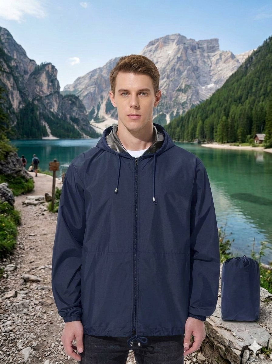 A man wearing a navy blue hooded rain jacket stands in front of a scenic mountain lake landscape, with a matching navy blue drawstring bag placed on the stone beside him. big green bear