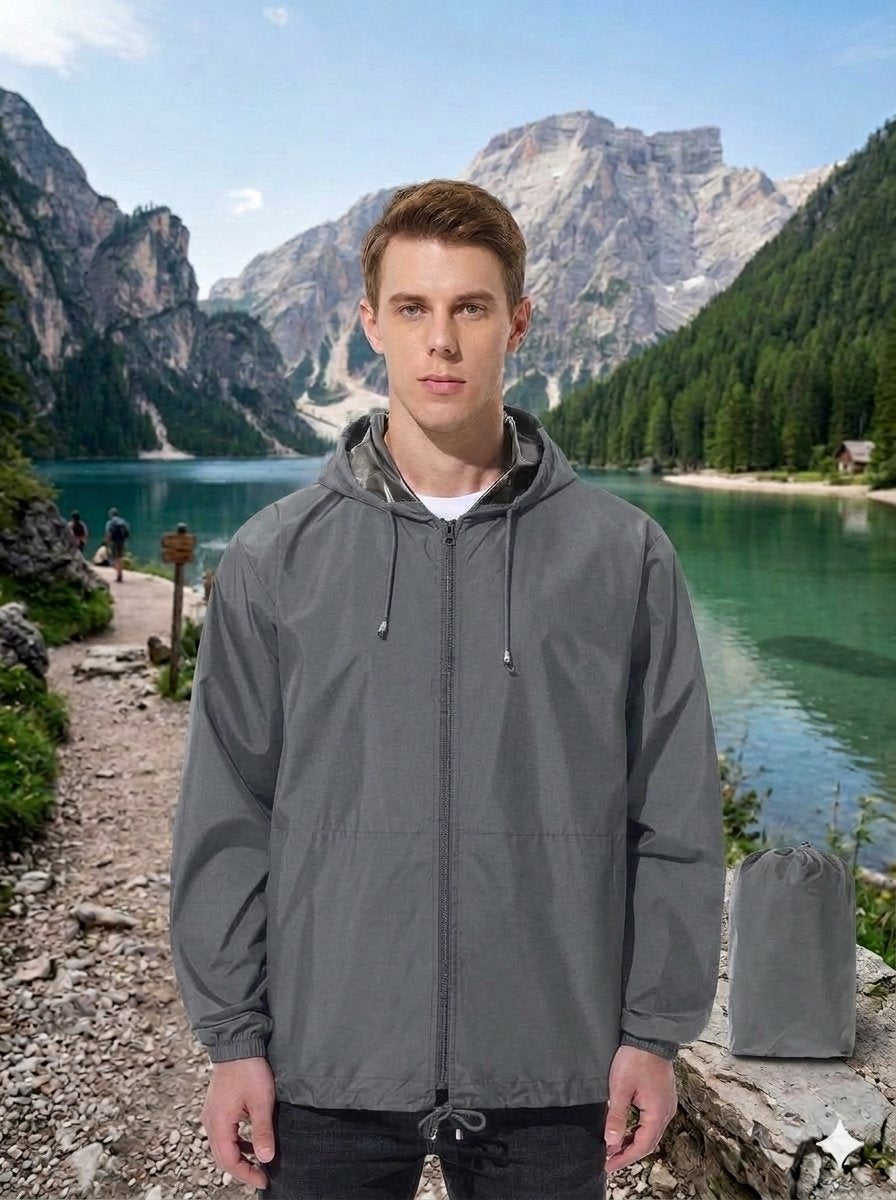 A man wearing a gray hooded rain jacket stands in front of a scenic mountain lake landscape, with a matching gray rain pouch placed on the stone beside him. big green bear