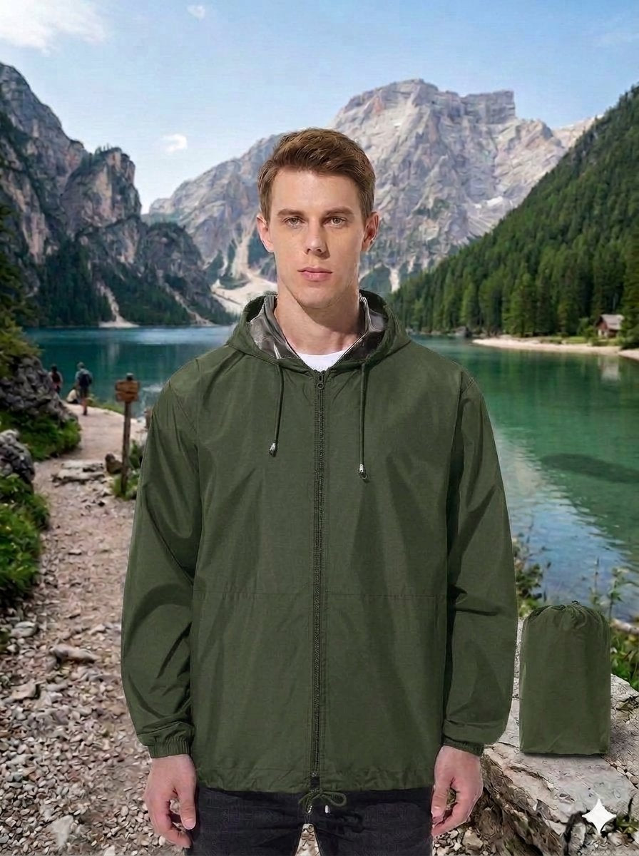 A man wearing an olive green hooded rain jacket stands in front of a scenic mountain lake background, with a matching green rain bag placed to his right. big green bear