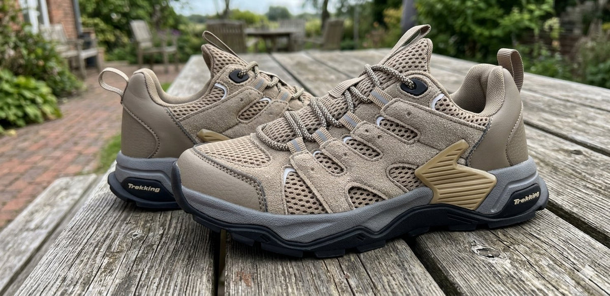 A pair of rugged outdoor sneakers in beige and gray with gold accents, displayed on a weathered wooden table with a garden background.