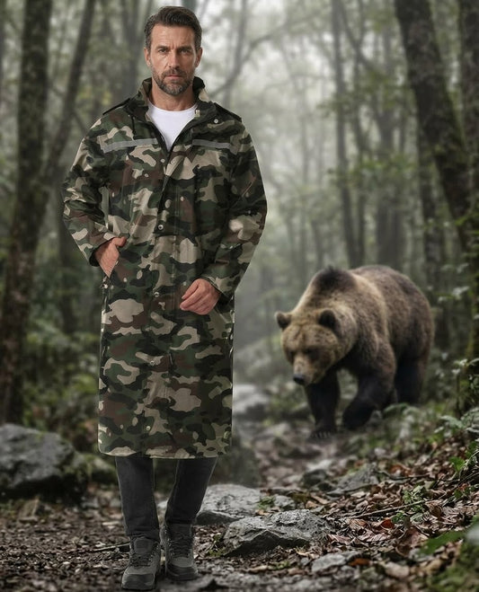A man wearing a long camouflage hooded raincoat stands on a forest path with a large brown bear walking behind him in a misty woodland setting. big green bear biggreenbear.com